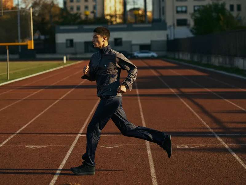 Sportler in dunkler Trainingskleidung läuft im Morgenlicht über eine leere Bahn