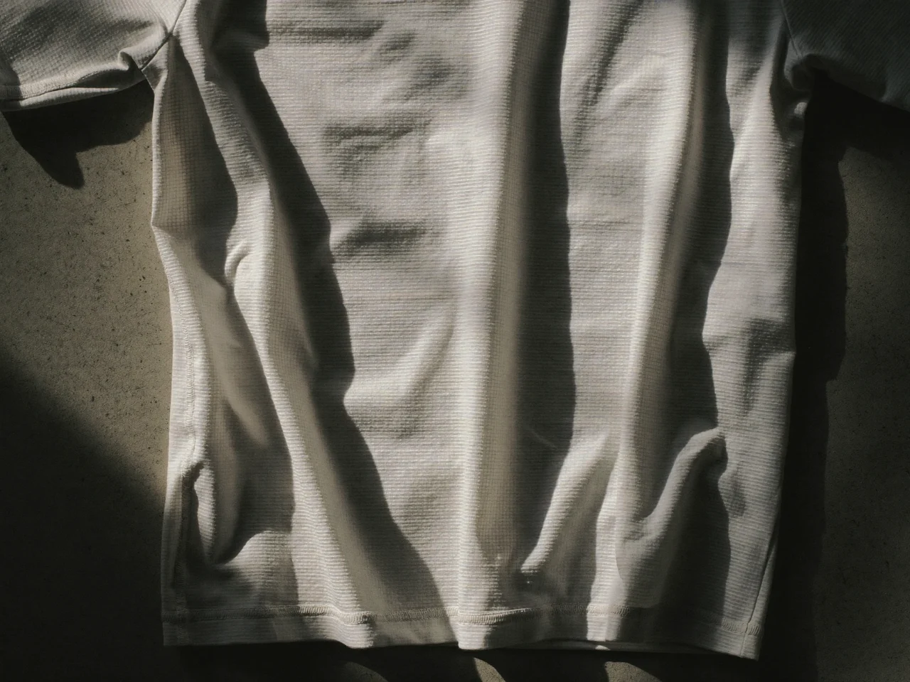 Technisches Mesh-Laufshirt flach auf heller Betonfläche, ohne Logo oder Aufdruck