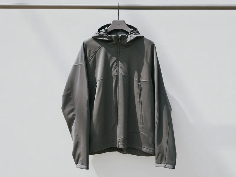 Leichte Laufjacke mit Kapuze an einer schlichten Metallstange vor weißer Wand