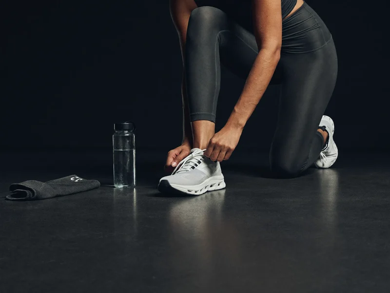 Person bindet Laufschuhe neben gefaltetem Sporttop und neutraler Trinkflasche